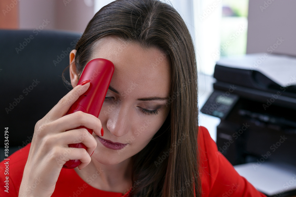 Dark-haired attractive business woman in red suit and red phone in hand suffering from headaches. The concept of hard work in the office. monochrome. Dark-haired attractive business woman in red suit and red phone in hand suffering from headaches. The concept of hard work in the office. monochrome.