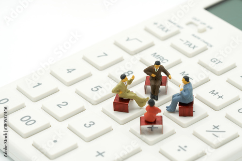 Miniature 4 people sitting on red staples placed on a white calculator. meeting or Discussion as background business concept with copy space. photo