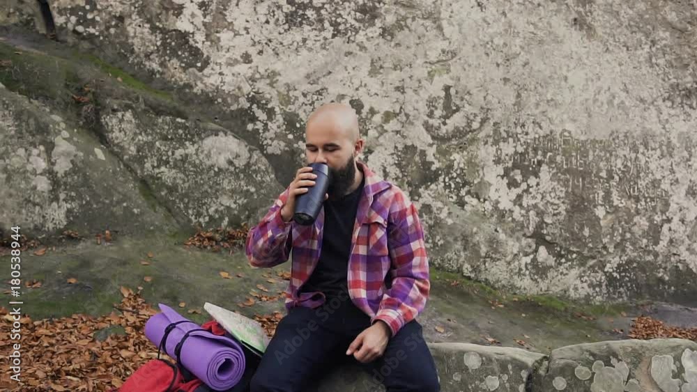 The tourist went to rest on a rock ,near a high cliff took out a warm cup of tea from the backpack, drink tea and enjoy the warm autumn weather