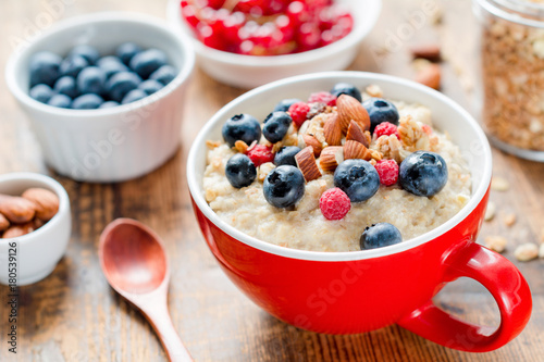 Oatmeal porridge bowl with blueberries, nuts and raspberries. Jar of granola on side. Healthy colorful breakfast for kids. Closeup view, selective focus