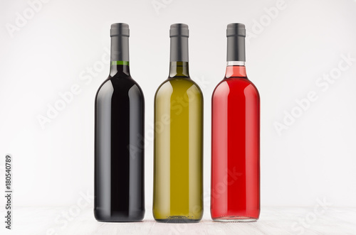 Three wine bottles different colors on white wooden board, mock up. Template for advertising, design, branding identity.