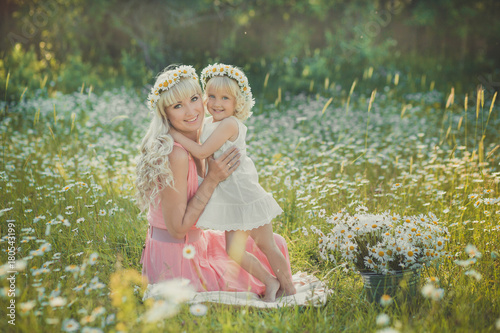 Magnificent picture of blond adorable lady woman mother mom in pink airy dress with daughter girl baby in white ambrace each other on daisy chamomile meadow with horse on background. photo