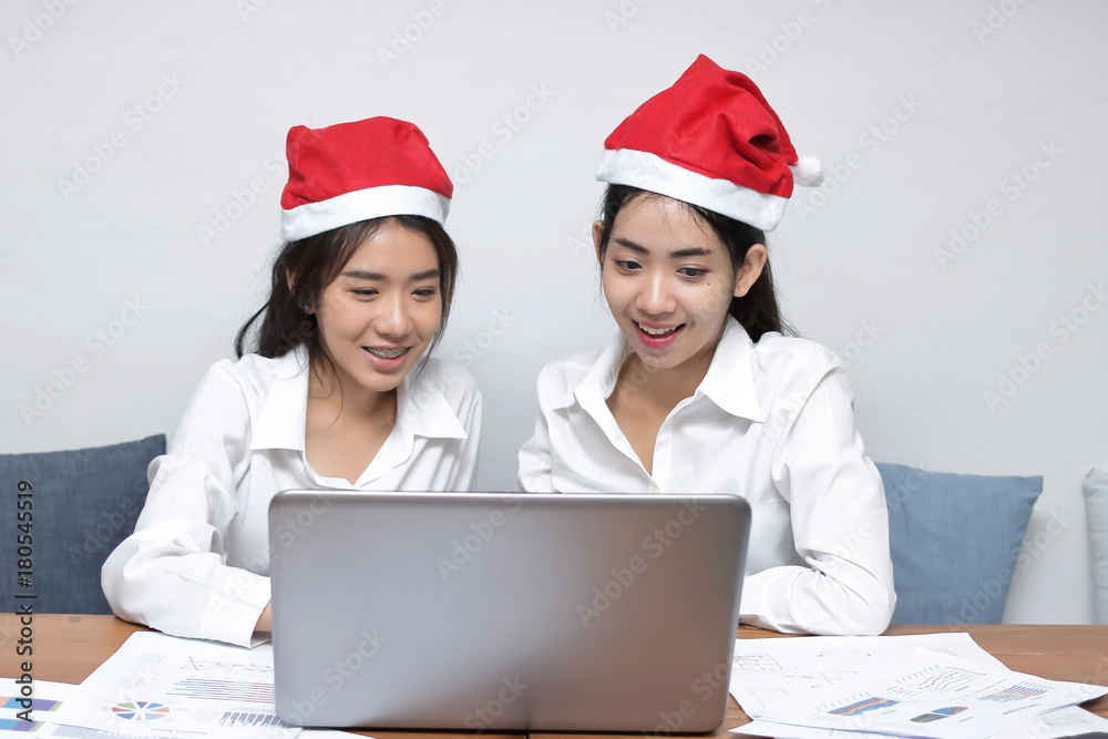 Happy young Asian business woman in Santa hats using laptop in office. Christmas or x-mas concept Happy young Asian business woman in Santa hats using laptop in office. Christmas or x-mas concept