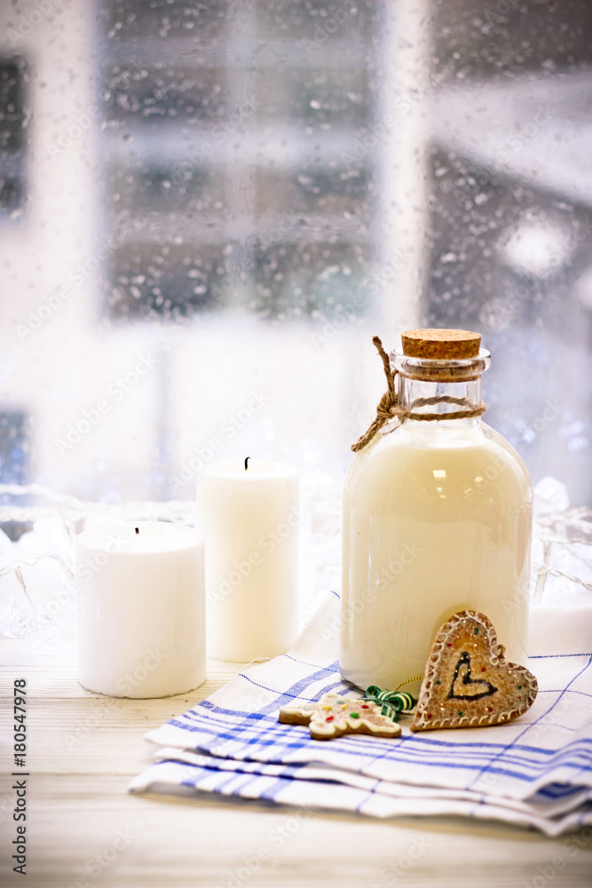 New Year's still life with a bottle of milk, biscuits, white candles, tablecloth in a box on a white wooden table, a country background in a clear sunny day New Year's still life with a bottle of milk, biscuits, white candles, tablecloth in a box on a white wooden table, a country background in a clear sunny day
