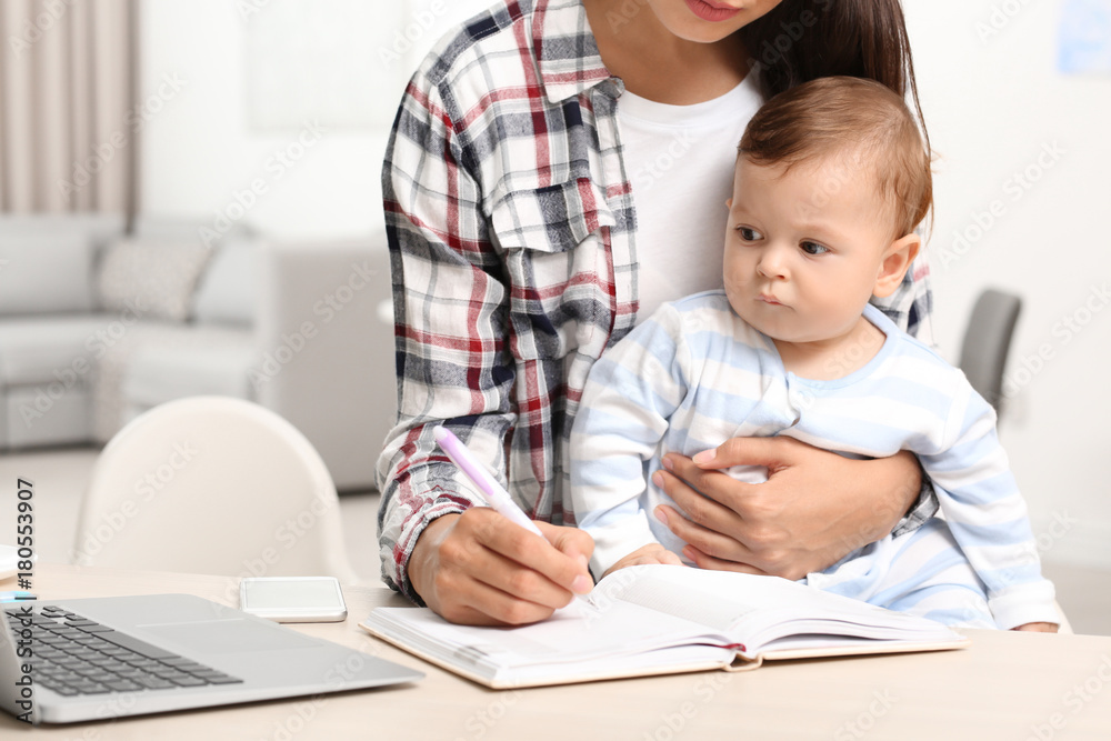 Young mother holding baby while working in home office Young mother holding baby while working in home office