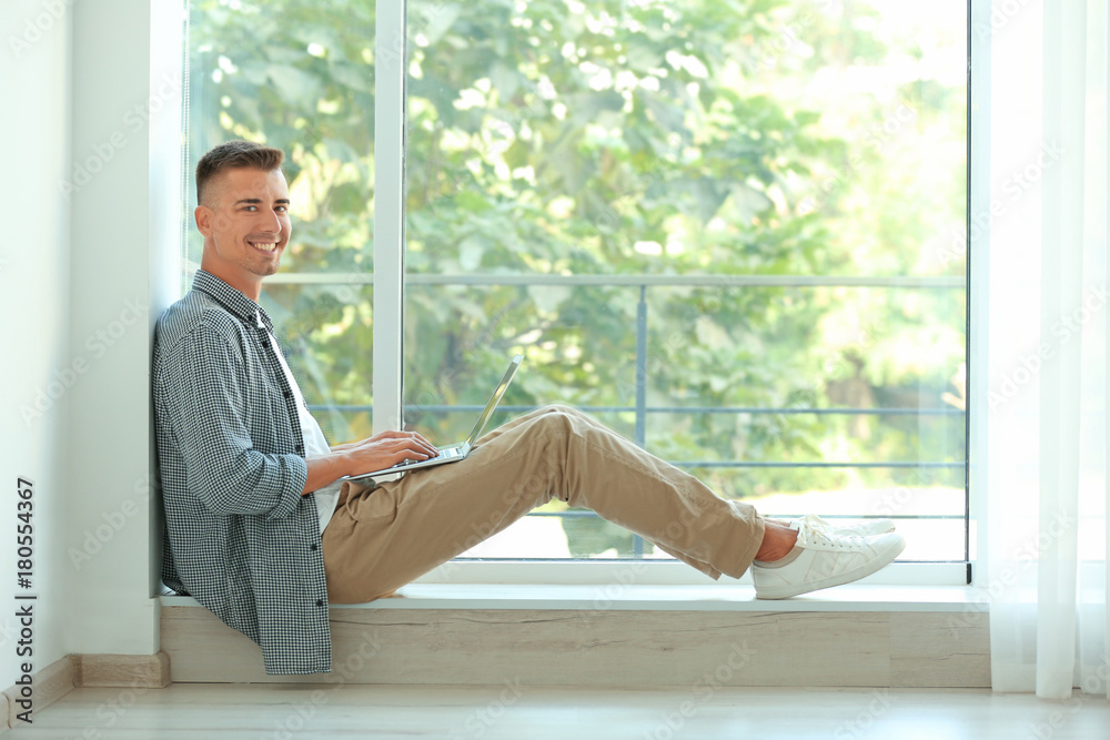 Young man using laptop near window at home