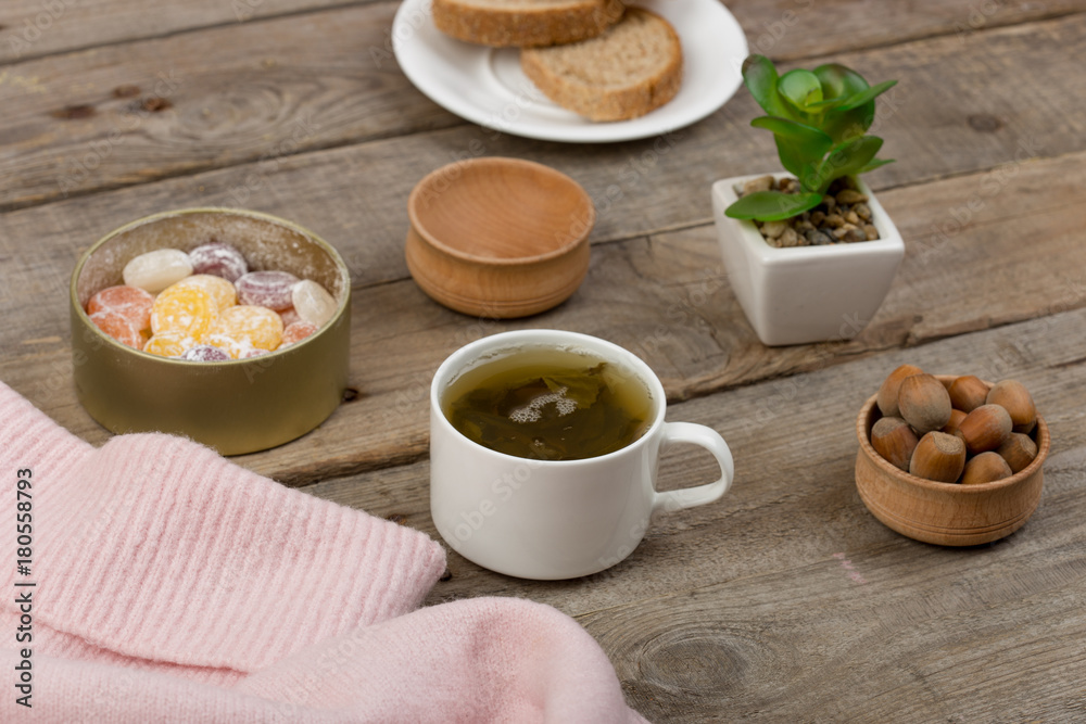 Winter cozy concept - the cup of tea, candy, nuts and pink sweater on brown wooden table Winter cozy concept - the cup of tea, candy, nuts and pink sweater on brown wooden table