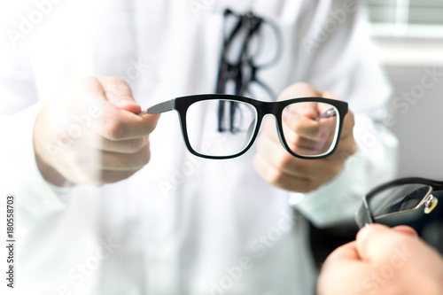 Optician showing new glasses to customer for trying. Eye doctor giving patient lenses.