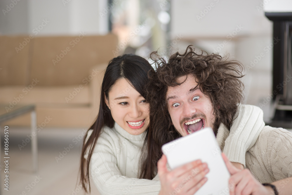multiethnic couple using tablet computer in front of fireplace multiethnic couple using tablet computer in front of fireplace