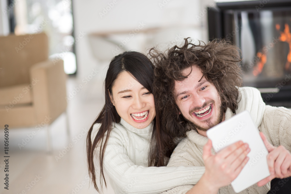 multiethnic couple using tablet computer in front of fireplace multiethnic couple using tablet computer in front of fireplace