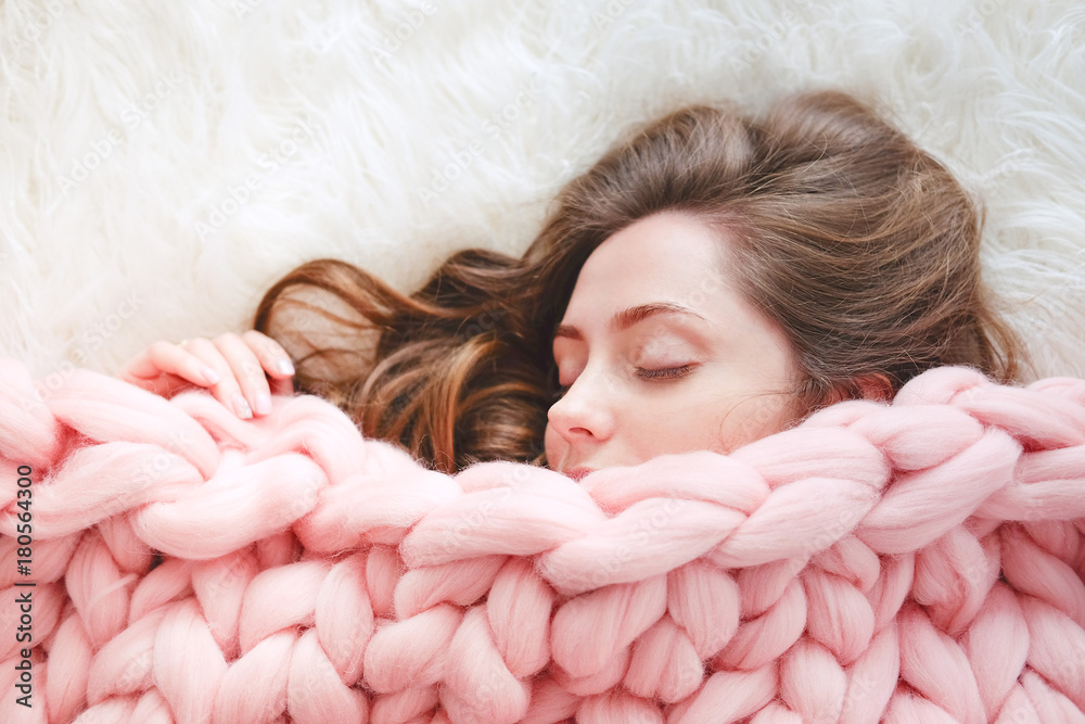 Young woman sleeping under warm peach color throw blanket