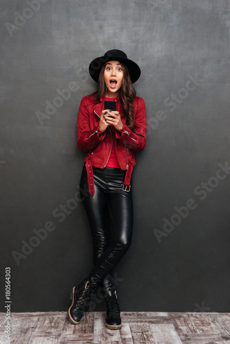 Surprised young woman wearing hat chatting by mobile phone