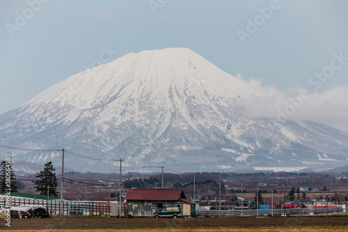 Close up Mount Yotei (inactive stratovolcano) with village on the foot hill and snow cover on the ground in winter in Hokkaido, Japan.