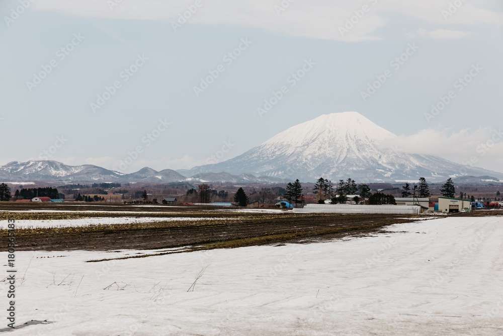 Mount Yotei (inactive stratovolcano) with village and snow cover on the ground in winter in Hokkaido, Japan.