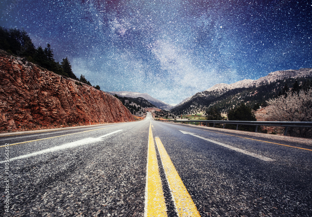 Asphalt road and lonely tree under a starry night sky and the Milky Way ...