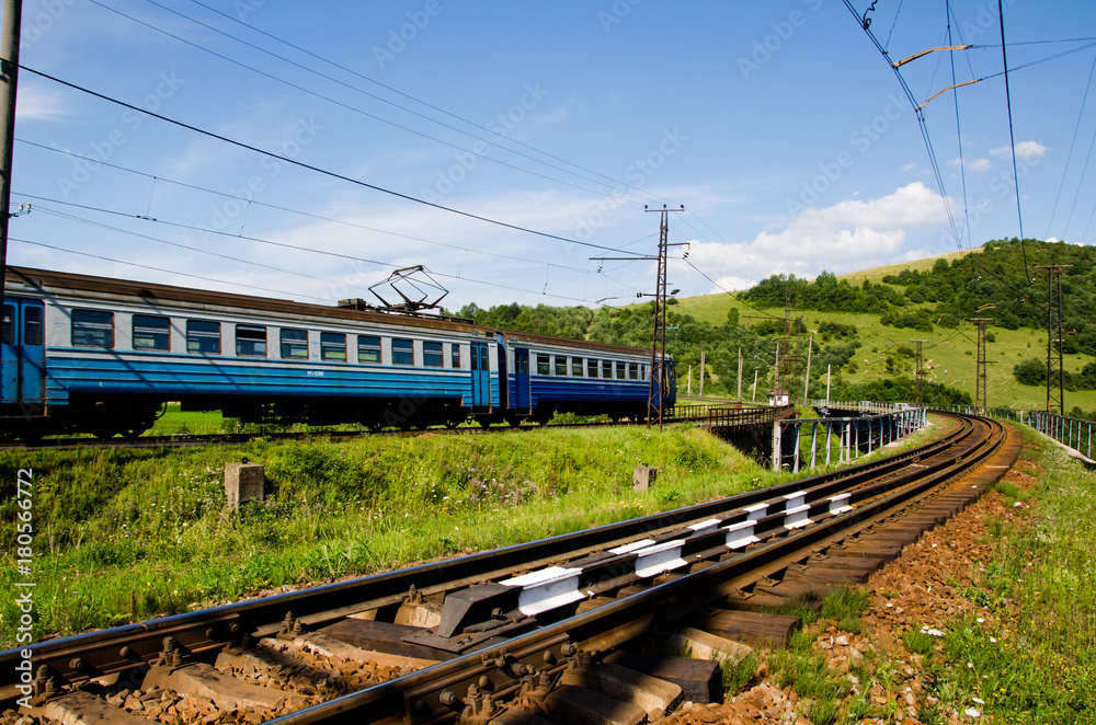 Naklejka premium The train travels by rail through the mountains