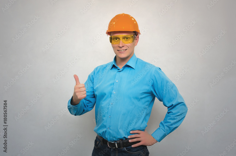 Young happy engineer worker in a helmet and protective glasses showing thumbs up gesture sign isolated. Construction people. Young happy engineer worker in a helmet and protective glasses showing thumbs up gesture sign isolated. Construction people.