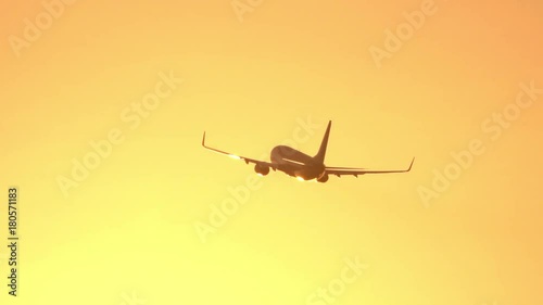 CLOSE UP: Passenger airplane flying at golden sunset. Airliner jet flying against the sunny golden sky at sunrise. People flying home from summer vacation travel by plane. Cargo plane shipping goods