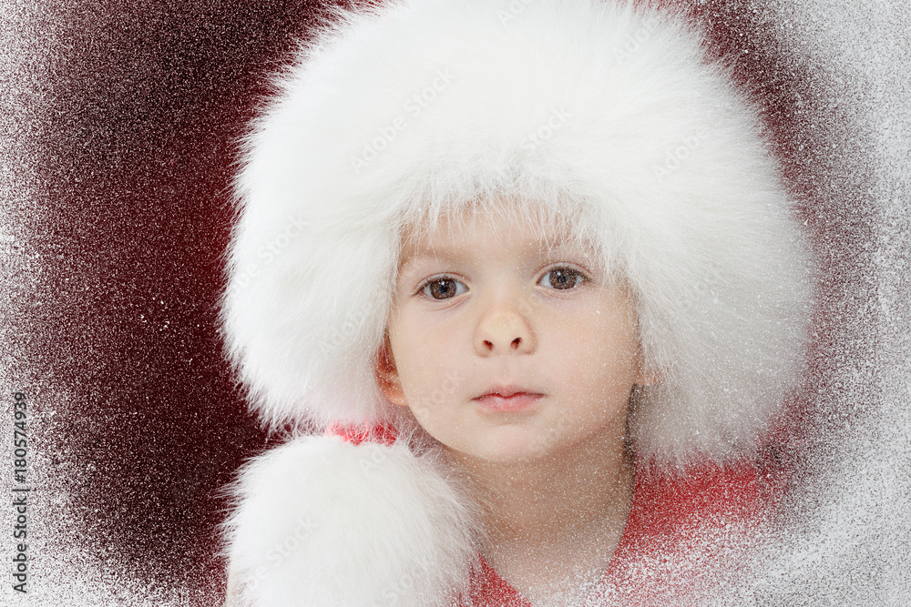 Merry Christmas little sad child on window looking at the winter. Kid and snowfall.