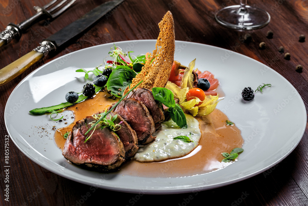 Delicious medium rare meat steak with sauce and salad on a plate. Healthy food made of meat fillet and fresh herbs on a wooden table.