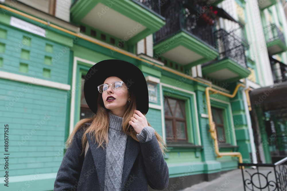 Portrait of a stylish woman in glasses and hats on the background of the architecture of the old town. A beautiful girl poses against the backdrop of old architecture.