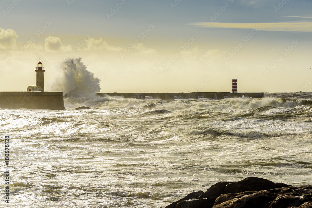 Landscape seascape lighthouse battered by huge waves on Atlantic Ocean with blue green skies and puffy clouds. 