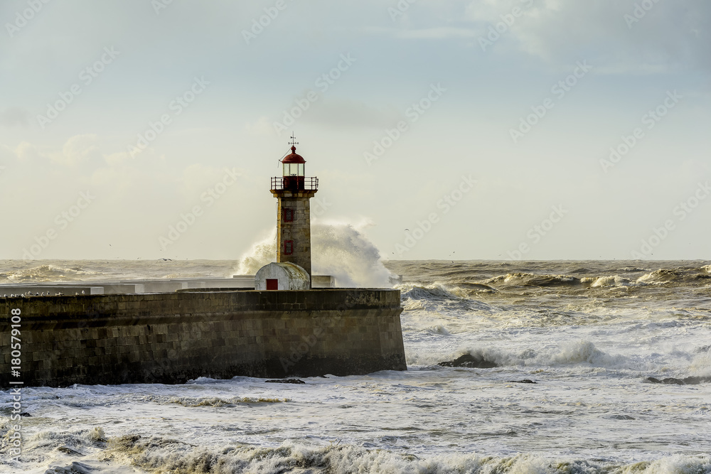 Landscape seascape lighthouse battered by huge waves on Atlantic Ocean with blue green skies and puffy clouds. 