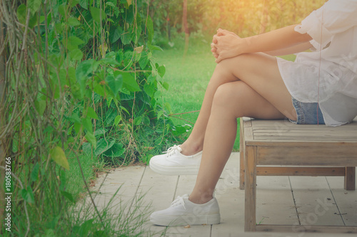 Relaxation Concept : Woman wear white shirt and short jean, her relaxing on wooden chair at outdoor garden surrounded with green natural sunlight in the background.