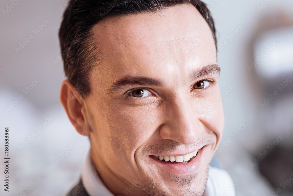 Obraz premium Sincere person. Positive brunette keeping smile on his face and looking forward while being at home