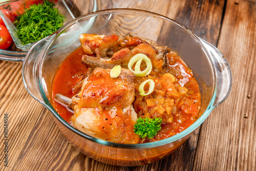 Roasted rabbit with herbs, tomato sauce and glass of wine on a plate.