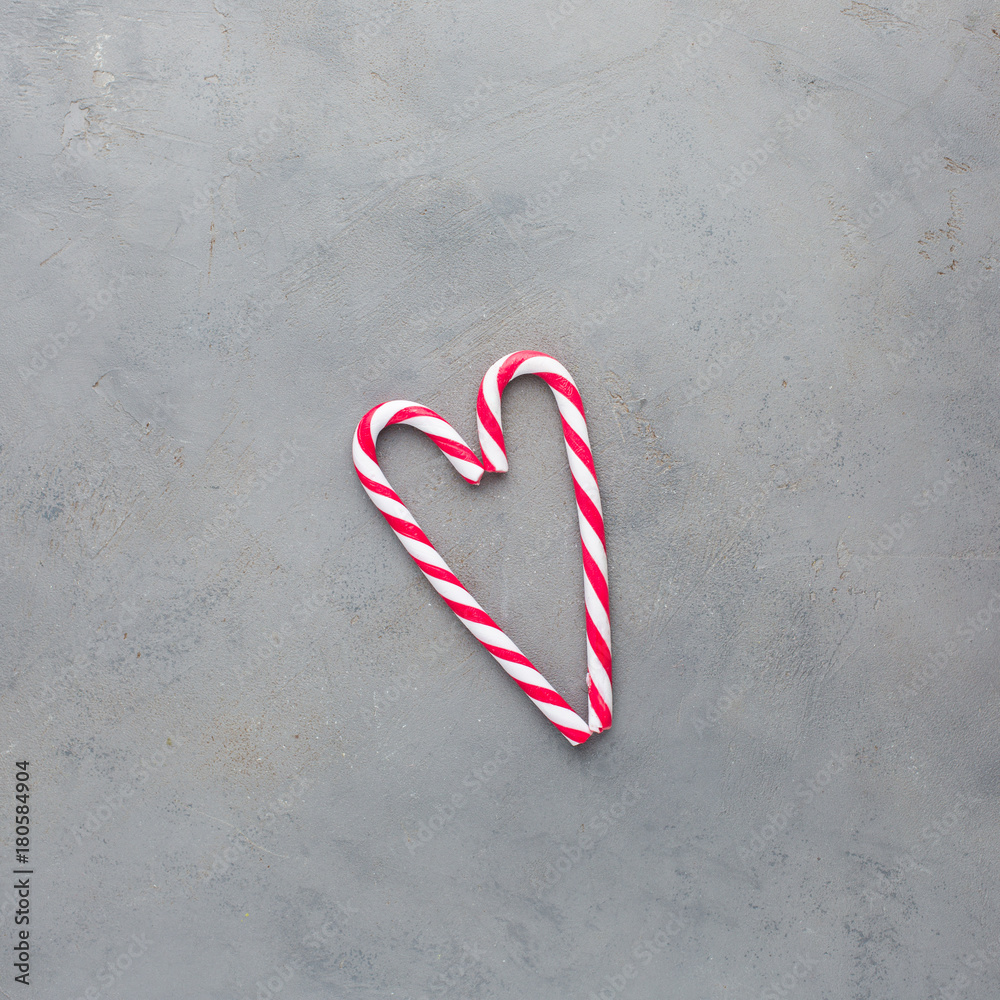 Heart of two red-white candy canes on the gray concrete background. Beautiful background. Flat lay, top view