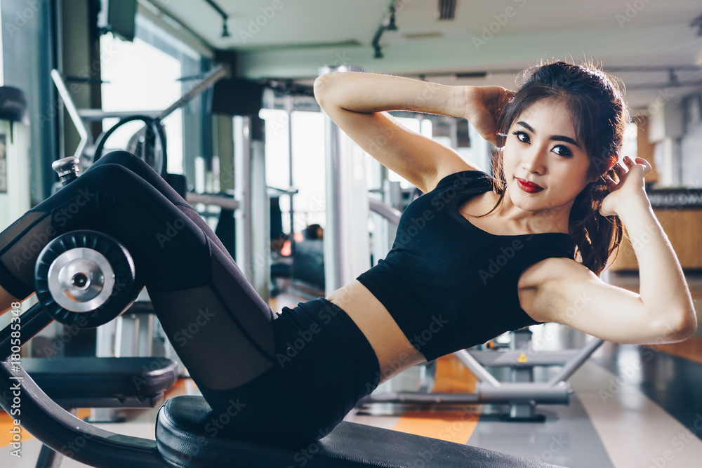 Fototapeta premium Asian woman exercising in the gym, Young woman workout in fitness for her healthy and office girl lifestyle. She is sit up position.