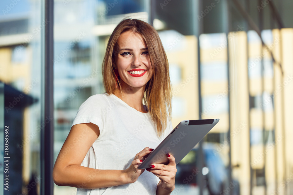 Cheerful girl wears white t-shirt use tablet pc sitting before modern building glass wall Cheerful girl wears white t-shirt use tablet pc sitting before modern building glass wall
