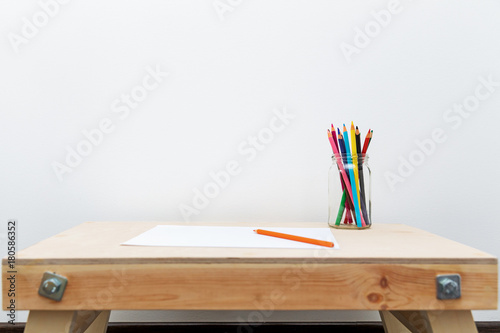 wooden child drawing table with color pencils by the white wall
