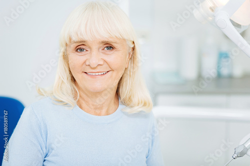 Caring about teeth. Close up of cheerful woman expressing satisfaction while sitting on dental chair and smiling at you