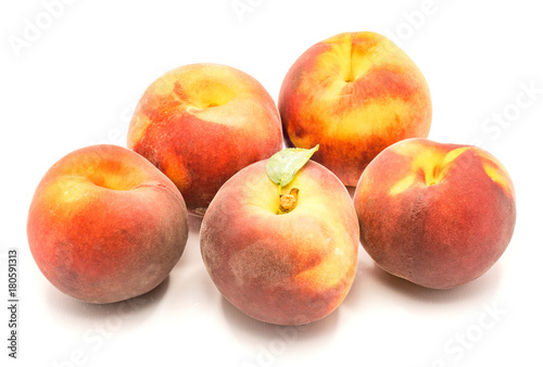 Group of five whole peaches, one with green leaf, isolated on white background.