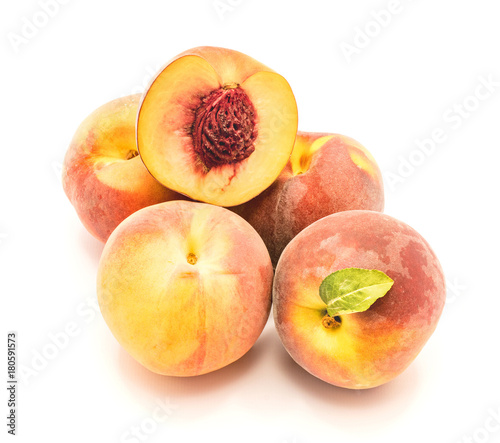 Folded peaches, one with green leaf and one sliced half with a stone, isolated on white background.