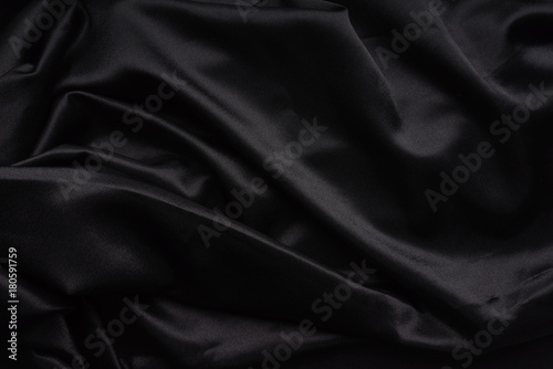 Dark black silky, satin fabric, wave, draperies. Beautiful textile backdrop. Close-up. Top view 