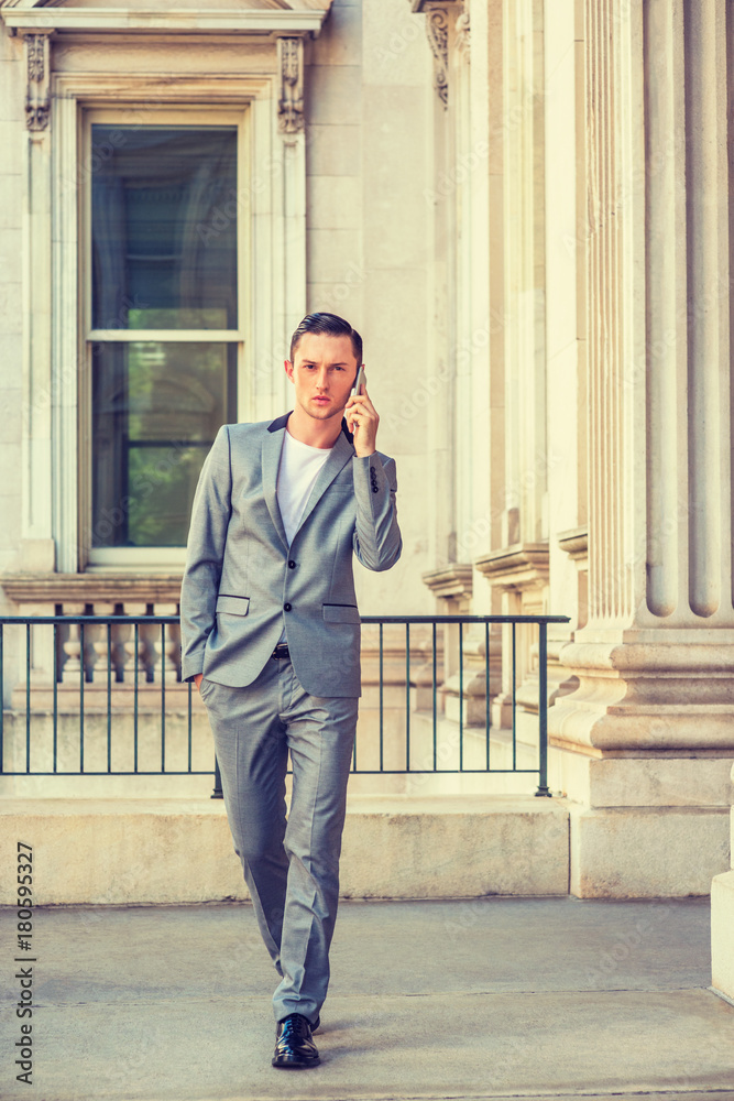 Eastern European Businessman working in New York. Wearing gray fashionable suit, leather shoes, hand put in pocket, a teacher walking inside vintage office building on campus, talking on cell phone.. Eastern European Businessman working in New York. Wearing gray fashionable suit, leather shoes, hand put in pocket, a teacher walking inside vintage office building on campus, talking on cell phone..