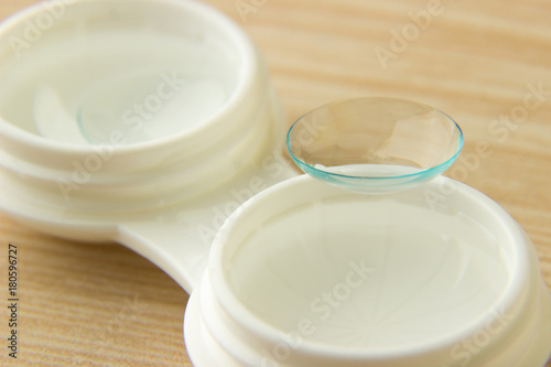 Contact lenses for the eyes and a white container with a solution on a wooden table