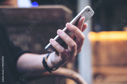 Closeup image of a woman's hands holding , using and looking at smart phone in modern cafe