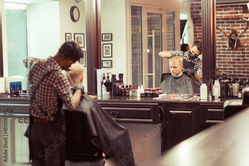 Handsome blonde man having his hair cut by hairdresser at the retro barbershop