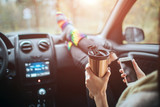 Autumn, Auto travel. Cose-up of a woman drinking take away cup coffee during the road trip in a car. Woman feet in warm socks on car dashboard. Drinking take away coffee and using a smartphone on road