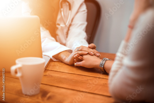 Doctor's hands holding female patient's hand for encouragement and empathy.
