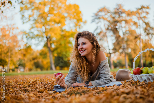 Portrait of a beautiful young woman laying in the autumn park.