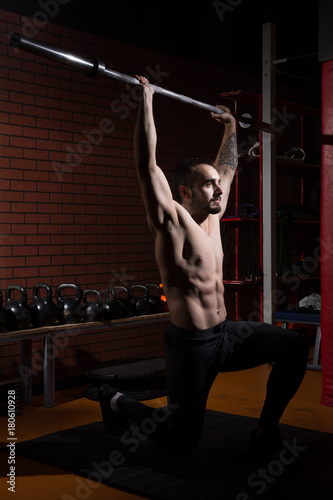 Young muscular man with a barbell bar in gym