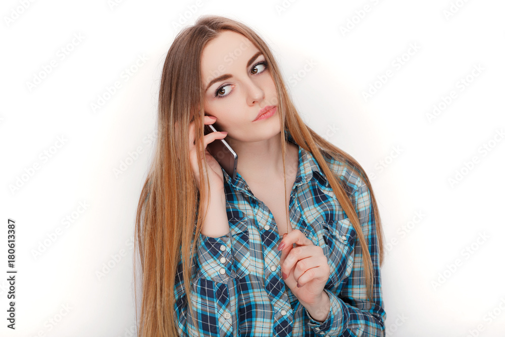 Portrait of a young adorable blonde woman in blue plaid shirt enjoying having emotional conversation on smartphone. Portrait of a young adorable blonde woman in blue plaid shirt enjoying having emotional conversation on smartphone.