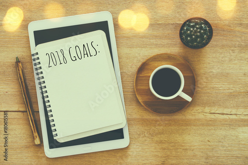 Top view 2018 goals list with notebook, cup of coffee on wooden desk.