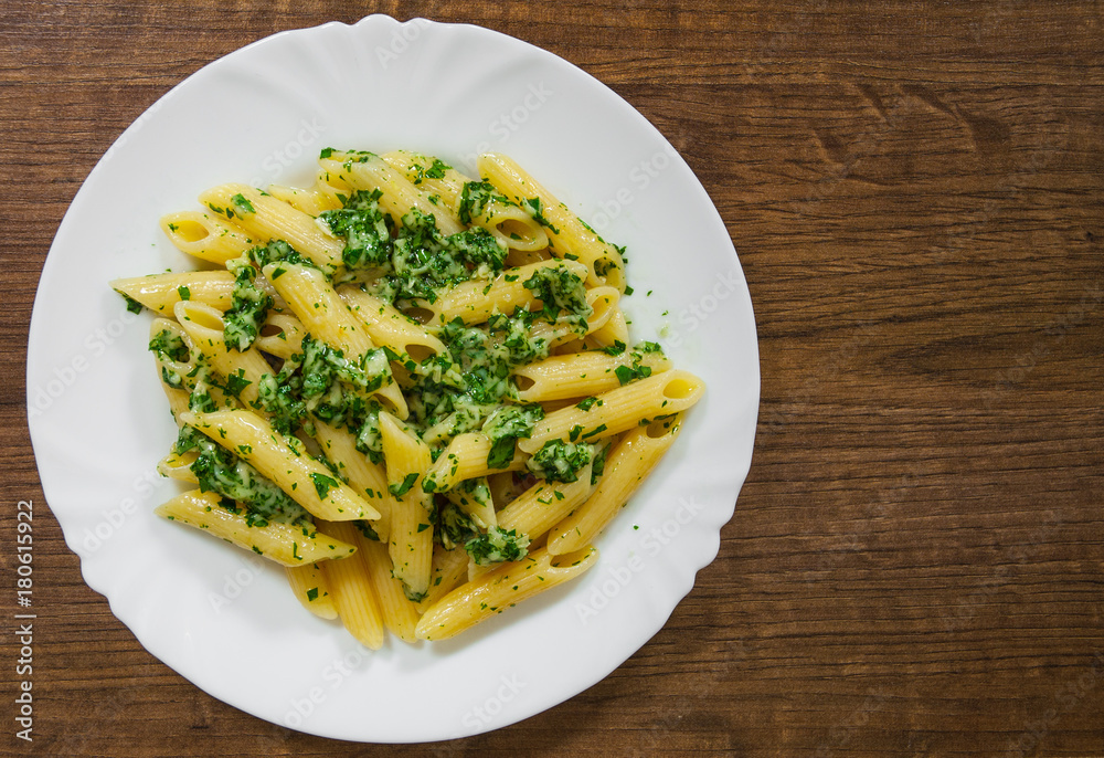 penne pasta with pesto sauce in plate on a wooden background. with copy space. top view