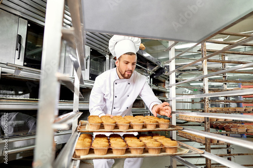 Baker man with a tray of cupcakes in his hands at work in Christmas. photo